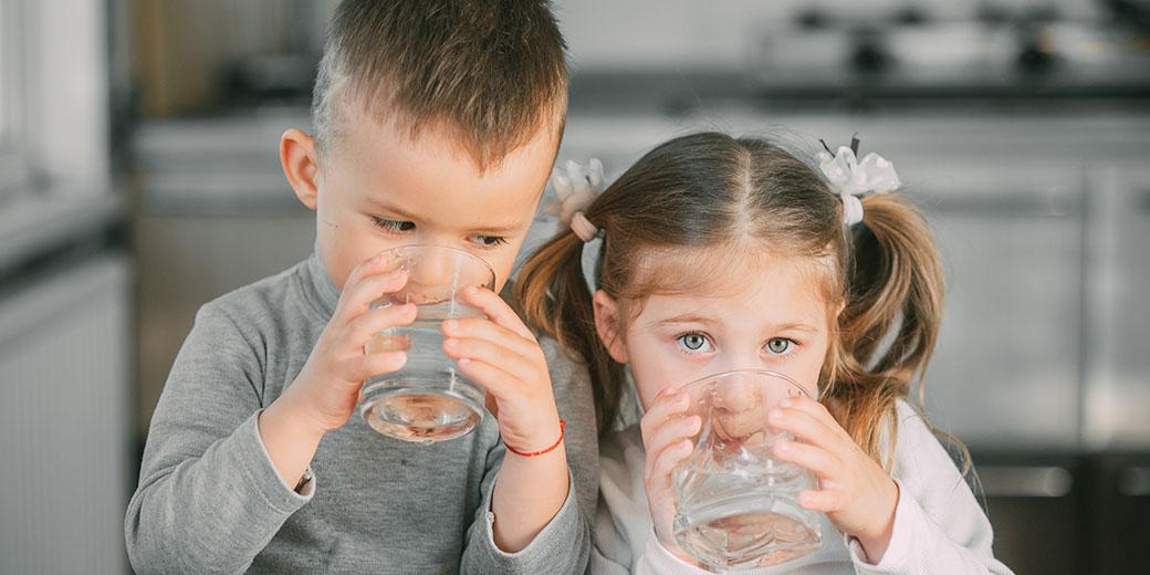 Two children drinking from glasses of water