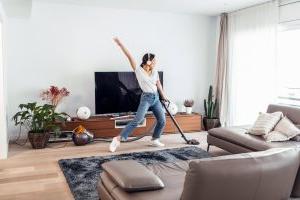 Young happy woman listening and dancing to music while cleaning the living room floor with a vacuum cleaner